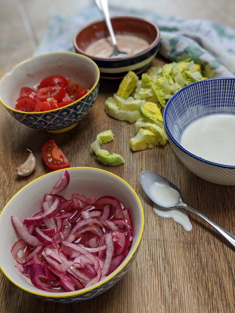 Sides in little bowls: Pickled red onion, shredded gem lettuce, seasoned sliced tomato, harissa mayonnaise