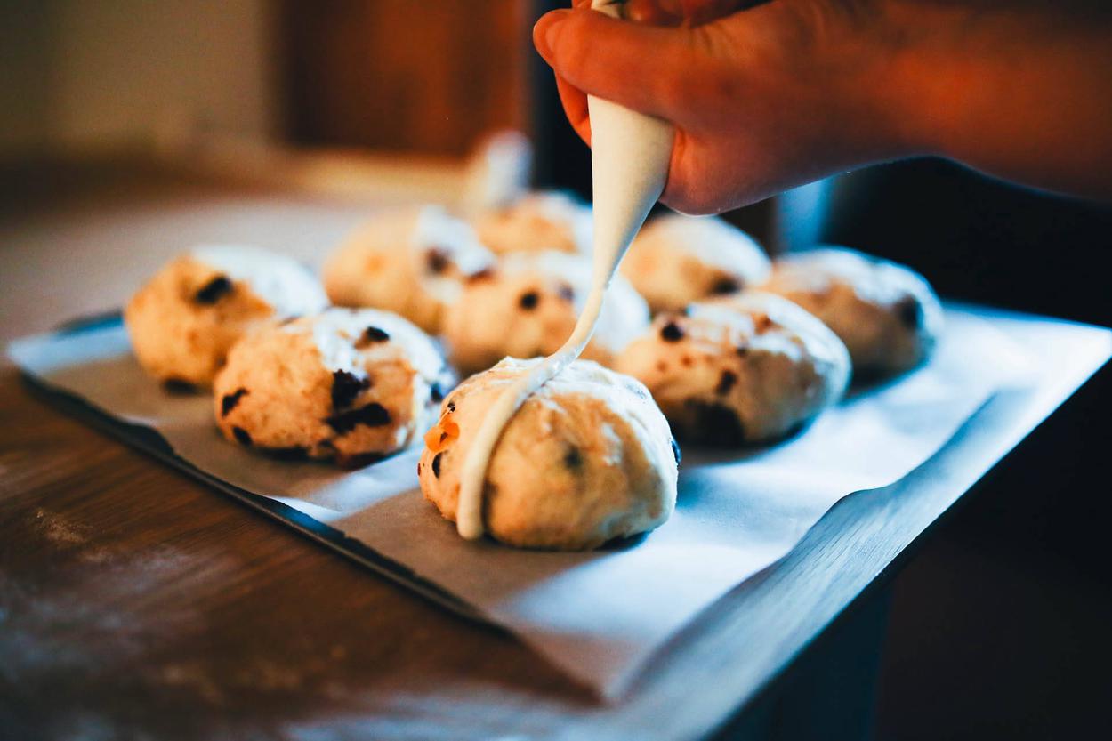 Crosses being piped onto unbaked hot cross buns